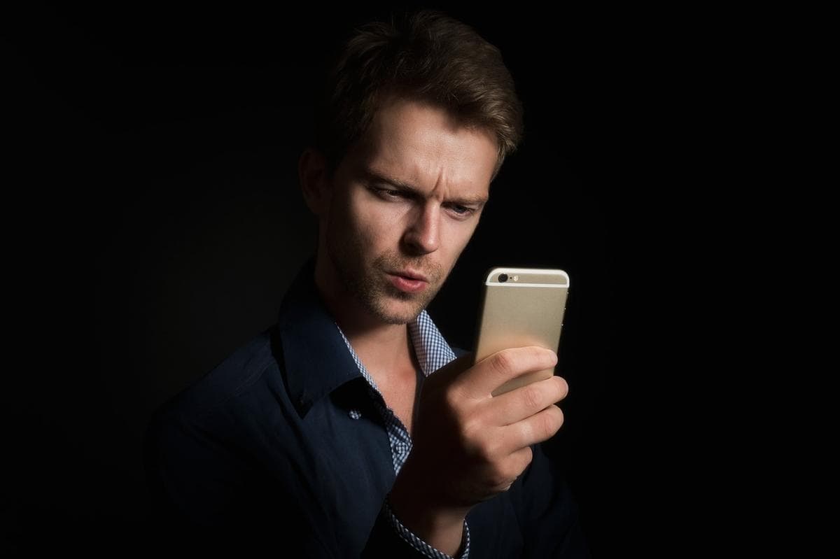 Un homme regardant attentivement l'écran d'un smartphone sur fond sombre