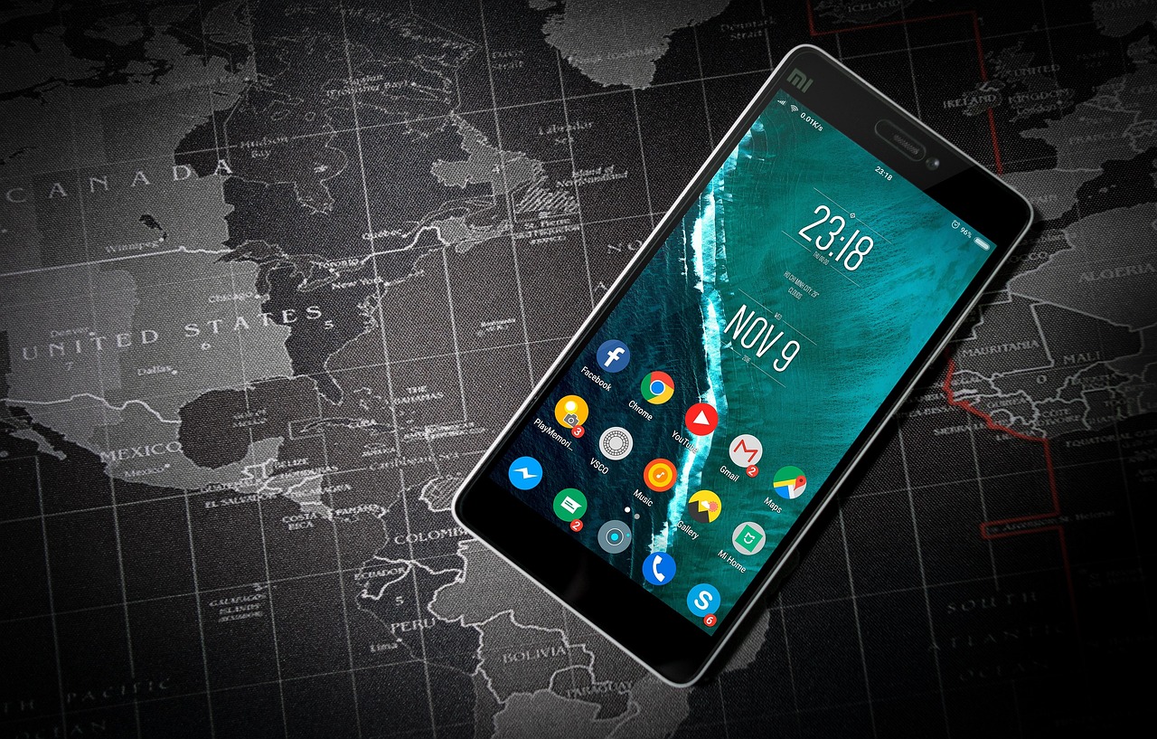 An Android phone home screen full of app icons, resting on a printed world map — both ChatGPT and Gemini ship mobile apps you can use anywhere.